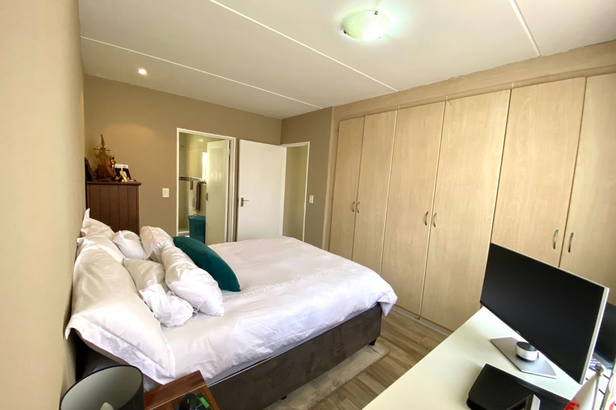 A functional bedroom featuring light wood-finish built-in cupboards, laminate flooring, and direct access to an en-suite bathroom.