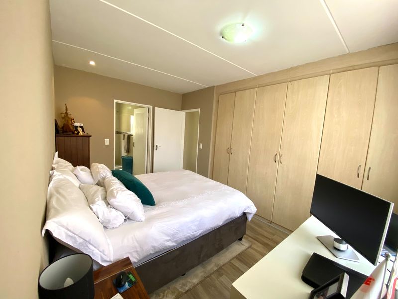 A functional bedroom featuring light wood-finish built-in cupboards, laminate flooring, and direct access to an en-suite bathroom.