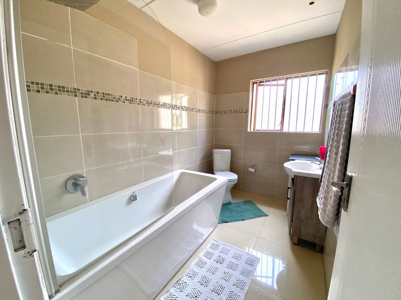 A well-maintained bathroom featuring a bathtub with a glass screen, a vanity basin, and neutral wall and floor tiling.