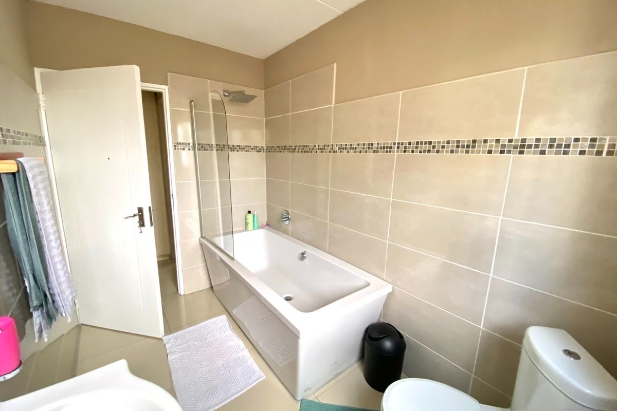 A functional bathroom featuring a bathtub with a glass shower screen, tiled walls with a decorative mosaic border, and a standard toilet.