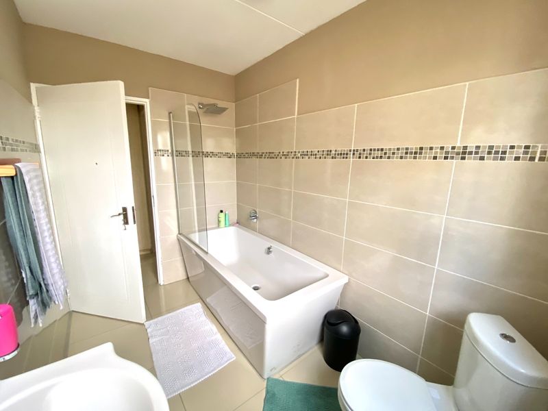 A functional bathroom featuring a bathtub with a glass shower screen, tiled walls with a decorative mosaic border, and a standard toilet.