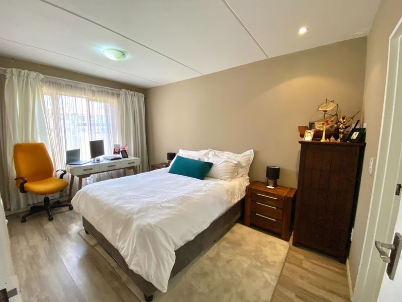 A well-maintained bedroom featuring light-toned laminate flooring, neutral wall finishes, and ample natural light through large windows.