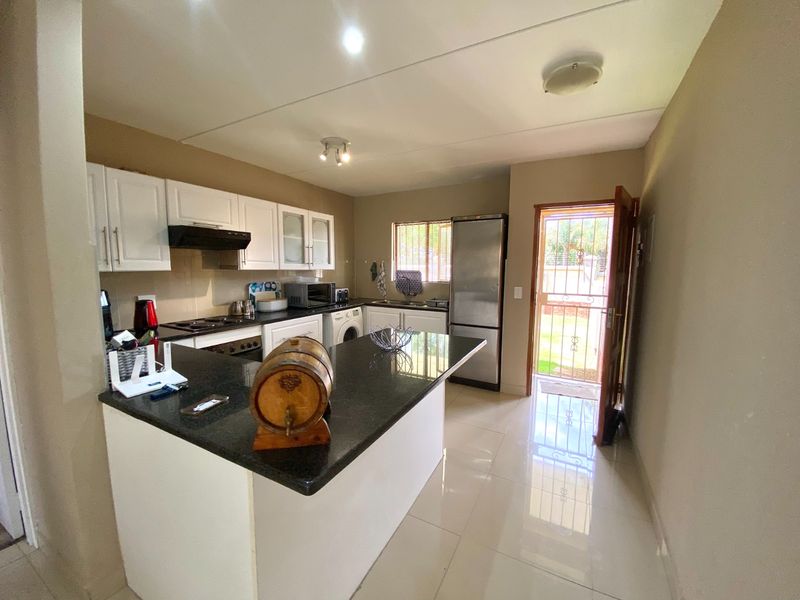 A functional kitchen featuring white cabinetry, granite countertops, built-in appliances, and tiled flooring, with direct access to the exterior.