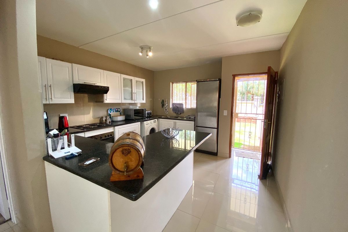 A functional kitchen featuring white cabinetry, granite countertops, built-in appliances, and tiled flooring, with direct access to the exterior.