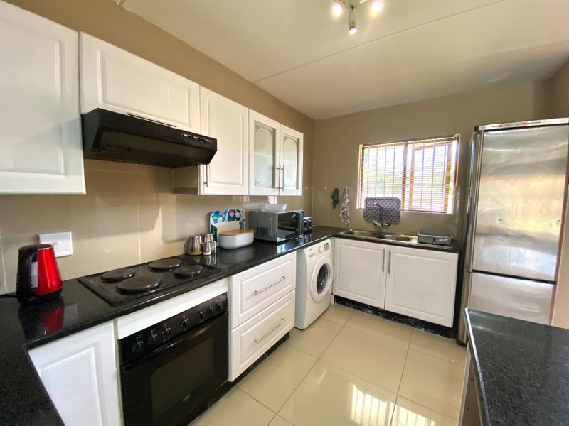 A functional kitchen featuring white cabinetry, granite countertops, built-in oven and hob, extractor fan, and tiled flooring with integrated laundry appliance space.