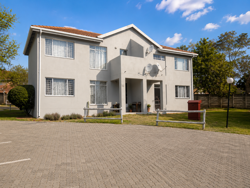 Front elevation of a two-story apartment building featuring a paved driveway, tiled roof, and communal garden area.