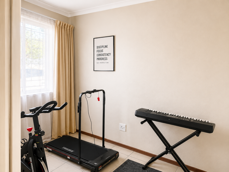 A well-maintained bedroom featuring neutral walls, tiled flooring, and a window with security bars, currently utilized as a home gym and music space.
