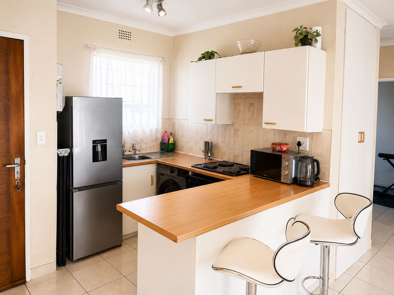 Compact kitchen featuring white cabinetry, laminate countertops, tiled backsplash, and a breakfast bar, providing a functional and efficient cooking and dining space.
