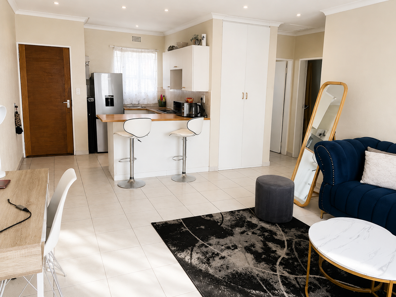 Open-plan living area featuring tiled flooring, a functional kitchen with a breakfast bar, and built-in storage cupboards.