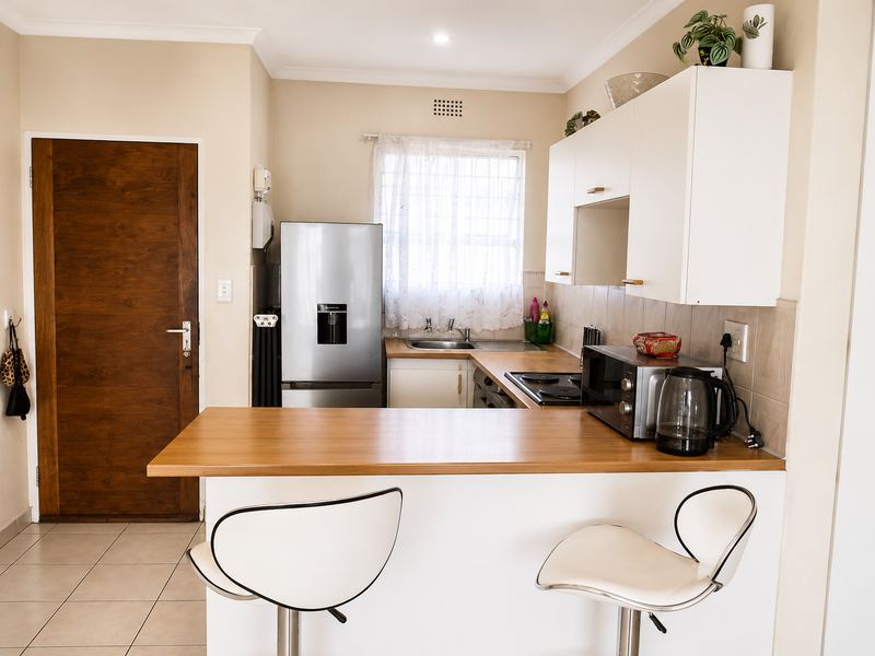 A functional kitchen featuring built-in cabinetry, a laminate breakfast bar, tiled backsplash, and a stainless steel sink, with a timber door leading to the space.