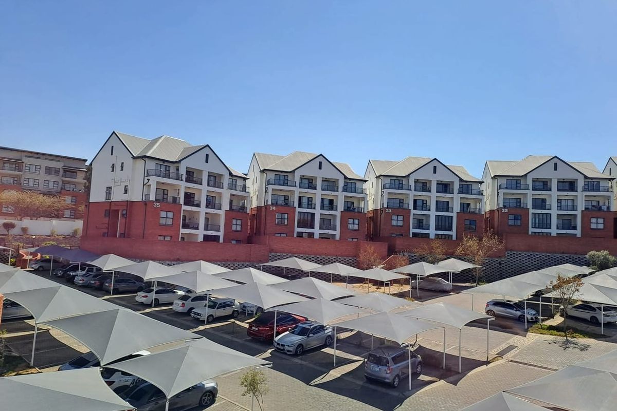 An elevated view of a townhouse complex featuring multiple residential blocks, paved parking areas, and extensive shade cloth carports.