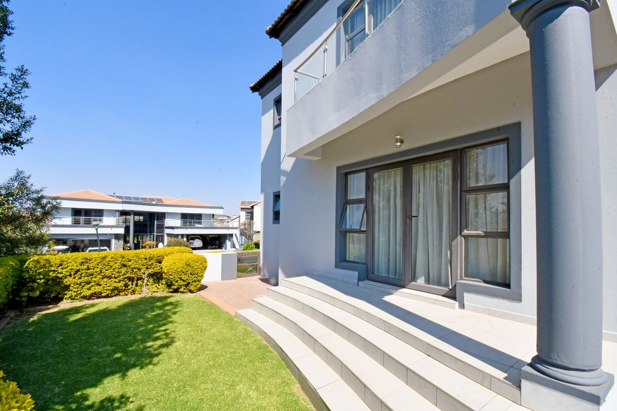 Rear view of the property featuring a tiled patio, concrete steps, and an upper-level balcony with glass balustrades overlooking a landscaped garden.