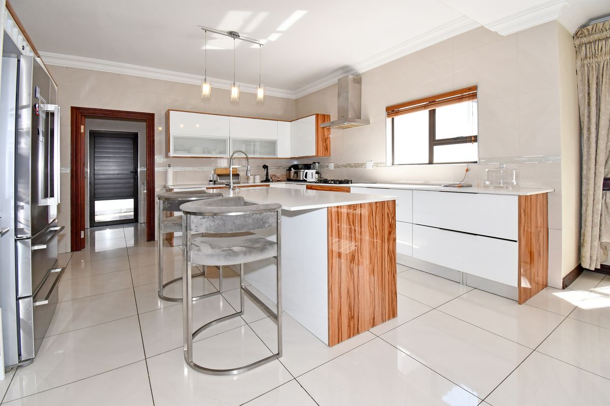 Modern kitchen featuring high-gloss cabinetry, a central island with stone countertops, stainless steel extractor fan, and polished tiled flooring.