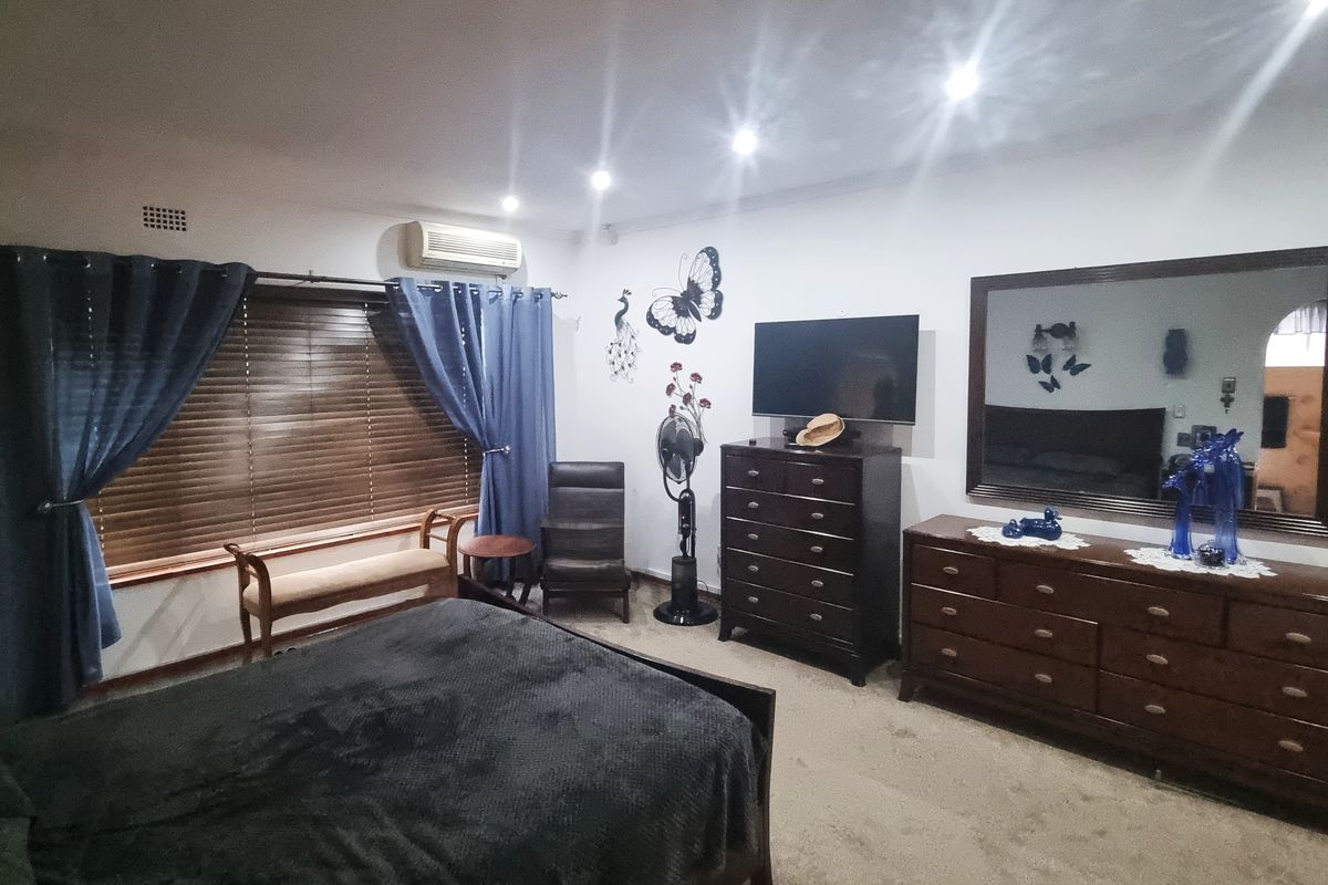 A spacious bedroom featuring carpet flooring, recessed downlighting, and a wall-mounted split-system air conditioner for climate control.