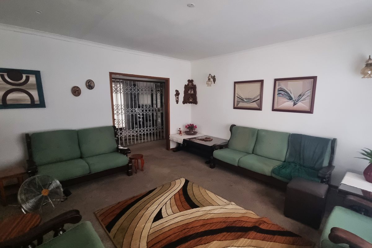 A spacious living room featuring carpeted flooring, wall sconces, and a secure metal gate leading to an adjacent area.