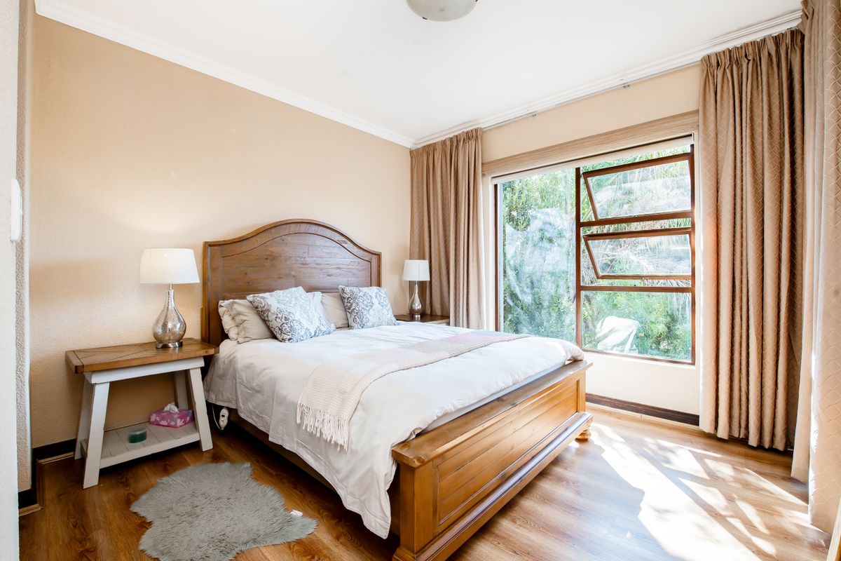 A well-maintained bedroom featuring timber-look flooring, coving, and a large top-hung window providing natural light and garden views.