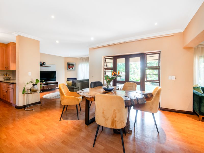 Spacious open-plan living and dining area featuring laminate flooring, recessed lighting, and direct access to the garden through timber-framed glass doors.