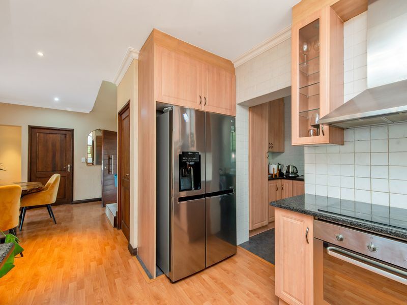 A well-maintained kitchen featuring light wood cabinetry, granite countertops, integrated appliances, and a tiled backsplash, leading into a secondary scullery area.