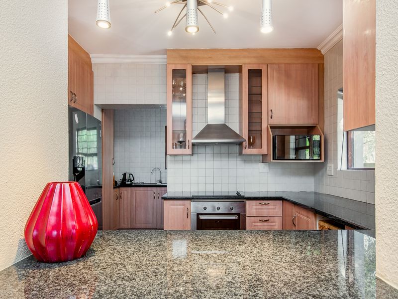 A functional kitchen featuring granite countertops, wooden cabinetry, a built-in oven, and a stainless steel extractor fan, with an adjacent scullery area.