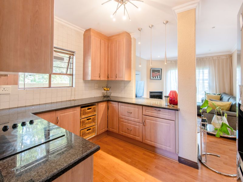 Open-plan kitchen featuring light wood cabinetry, granite countertops, and a tiled backsplash, seamlessly flowing into the adjacent living area.