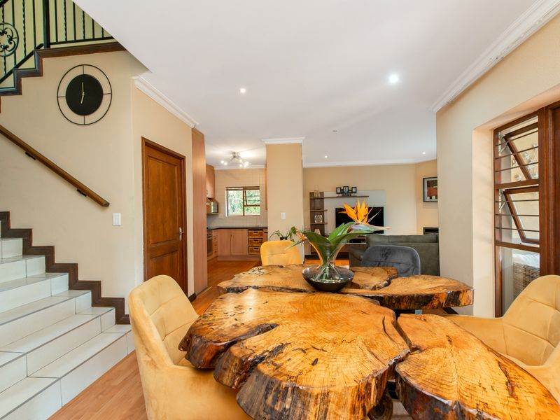 Open-plan living and dining area featuring a staircase with wrought iron balustrade, laminate flooring, and recessed lighting, flowing into the kitchen space.