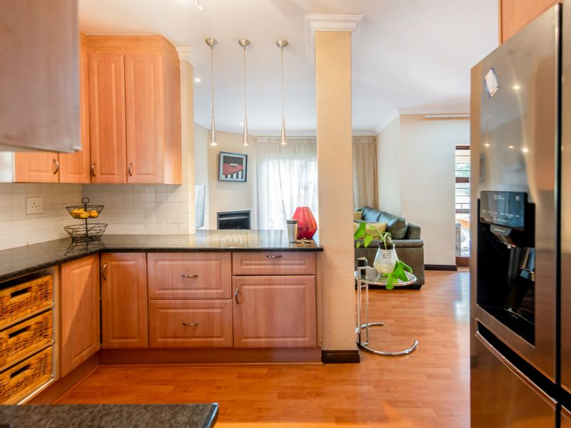 Open-plan kitchen and living area featuring warm-toned wooden cabinetry, granite countertops, laminate flooring, and a cozy built-in fireplace.