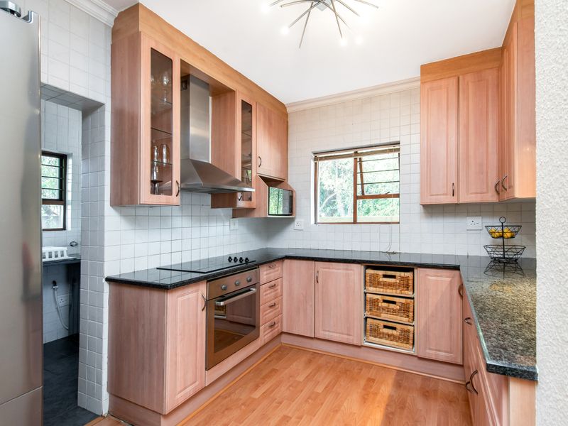 A functional kitchen featuring light wood cabinetry, granite countertops, built-in oven and hob, and a tiled backsplash, with an adjacent scullery area.
