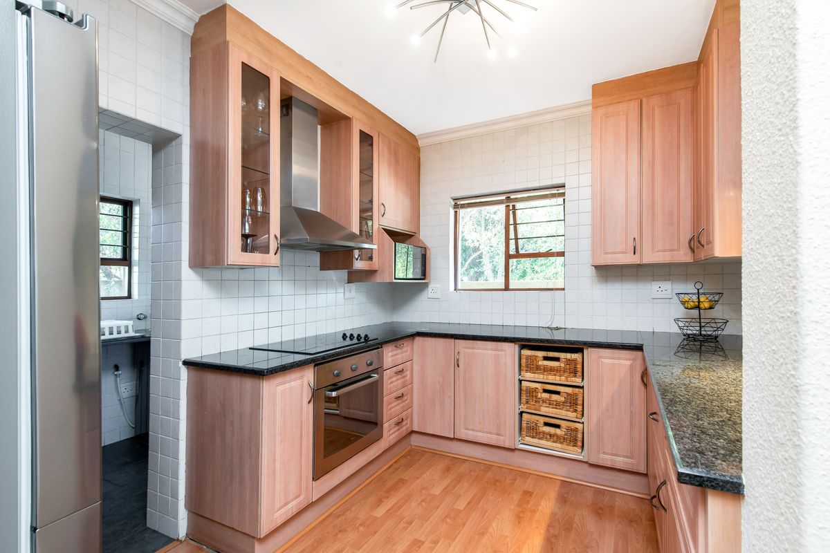 A functional kitchen featuring light wood cabinetry, granite countertops, built-in oven and hob, and a tiled backsplash, with an adjacent scullery area.