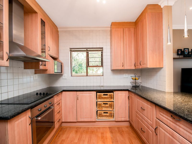 A functional kitchen featuring light wood cabinetry, dark granite countertops, a built-in oven, electric hob, and a tiled backsplash.