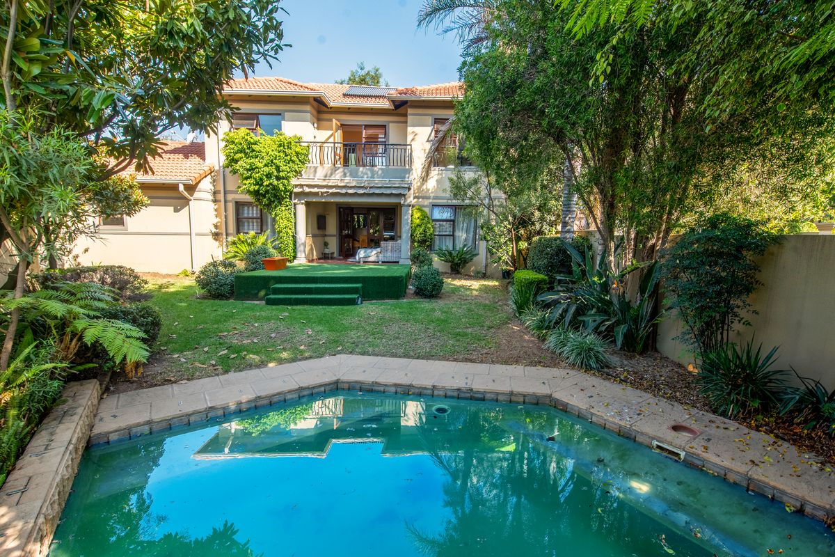 Rear view of a two-story house featuring a swimming pool, a raised terrace area, and a balcony overlooking the garden.