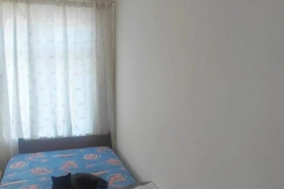 A simple bedroom featuring a window with curtains and a ventilation grille, providing a functional space with neutral wall finishes.