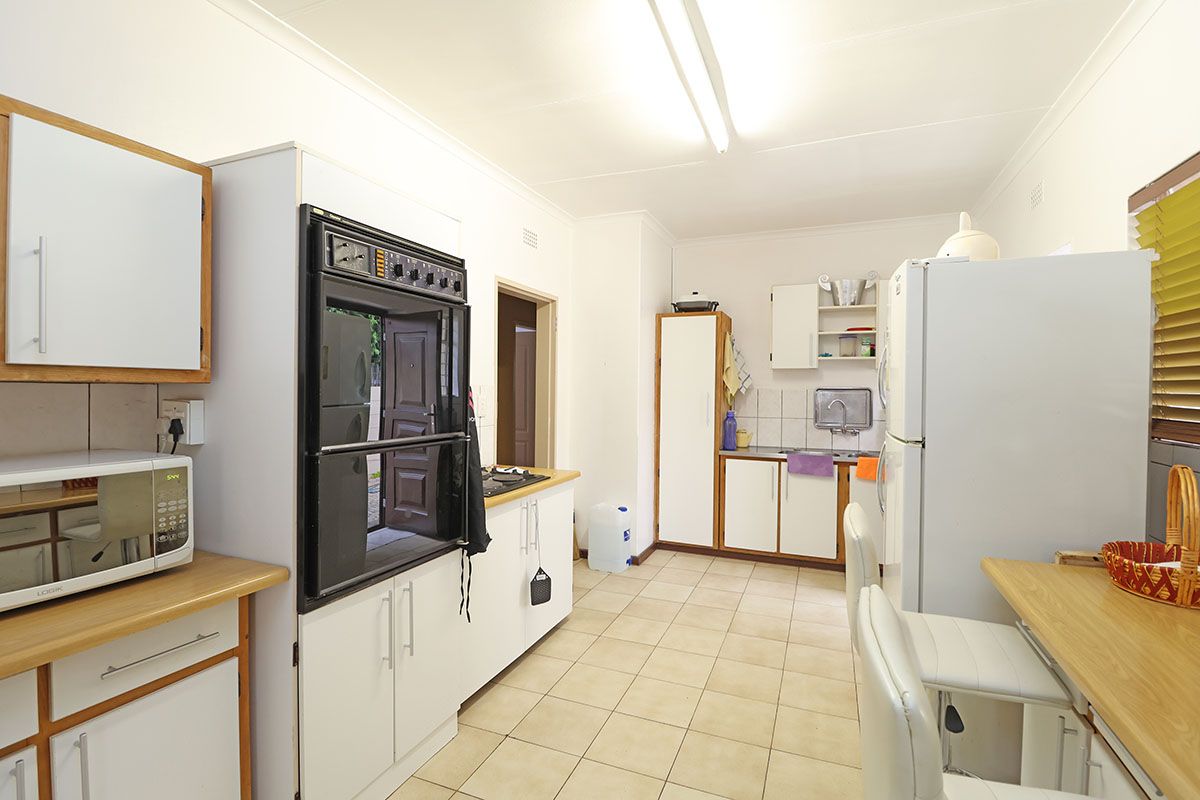 A functional kitchen featuring tiled flooring, laminate countertops, built-in oven, hob, and ample cabinetry, offering a practical layout with potential for modern updates.