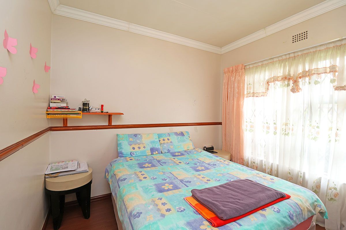 A bedroom featuring laminate flooring, crown molding, a chair rail, and a built-in wall shelf, offering a functional space with potential for cosmetic updates.