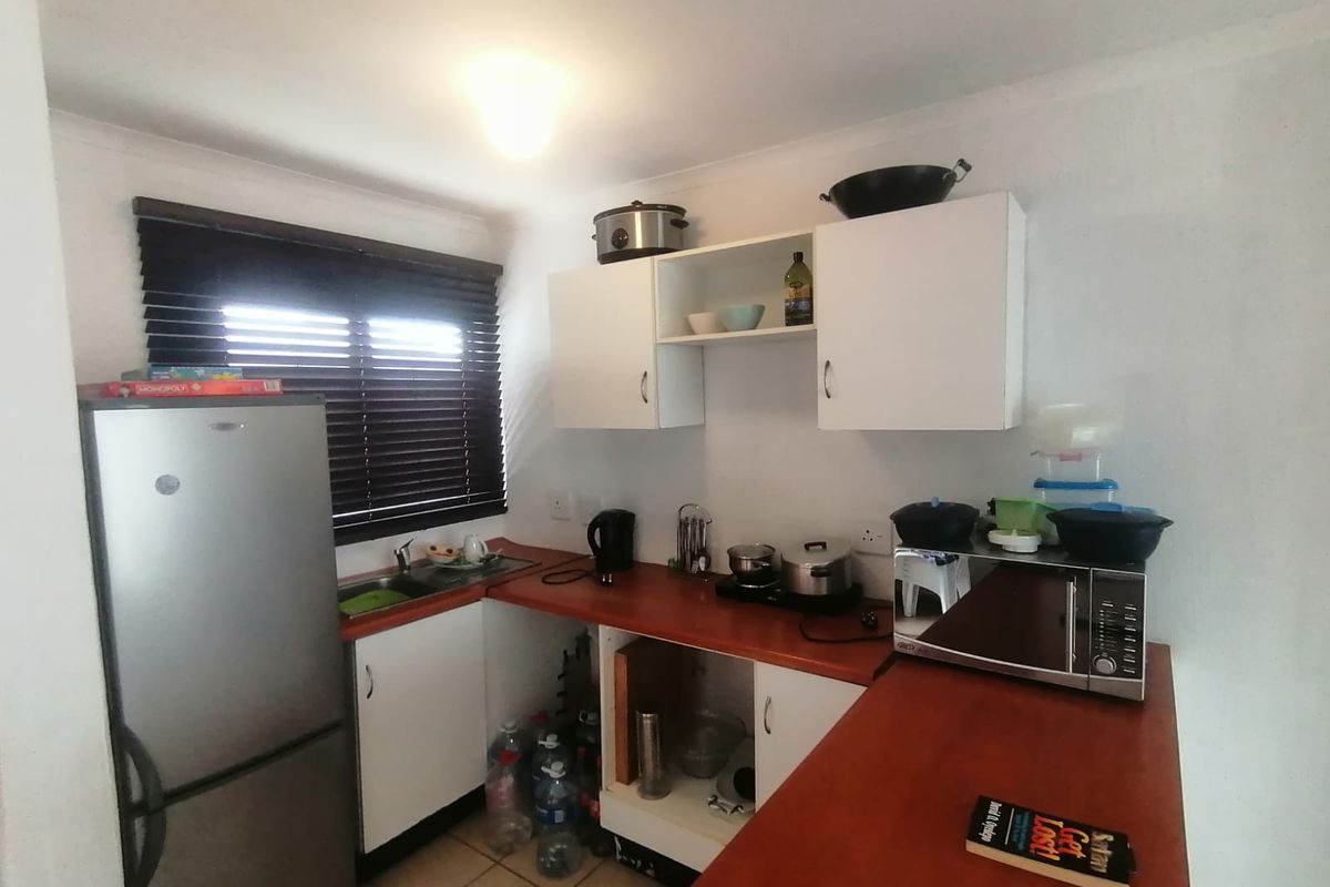 A compact kitchen featuring laminate countertops, white cabinetry, and a stainless steel sink, currently requiring minor repairs to the lower cabinetry.