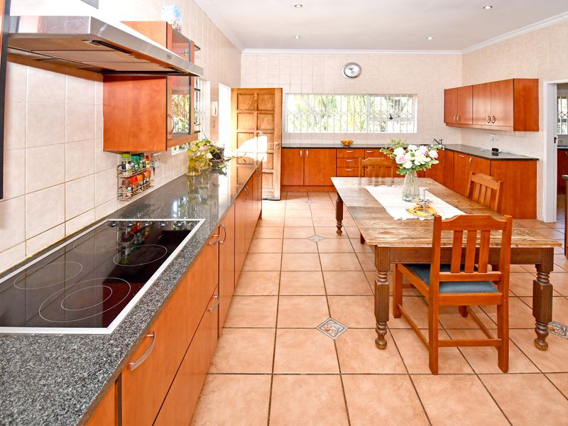 Spacious open-plan kitchen and dining area featuring granite countertops, extensive wooden cabinetry, an electric hob, and tiled flooring throughout.