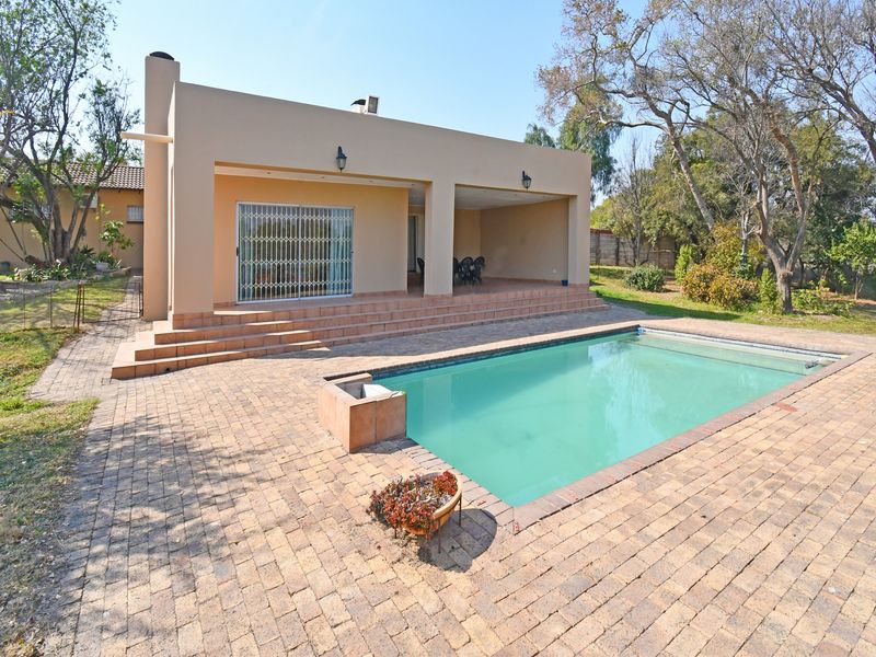 A spacious outdoor area featuring a swimming pool, brick-paved surround, and a covered patio with direct access to the home.