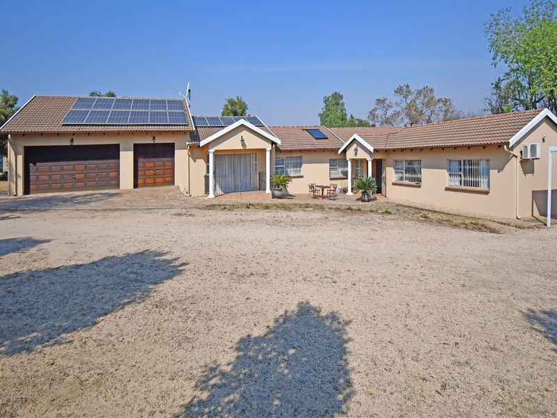 Front view of a single-story house featuring a double garage, solar panel installation, and a large gravel driveway.