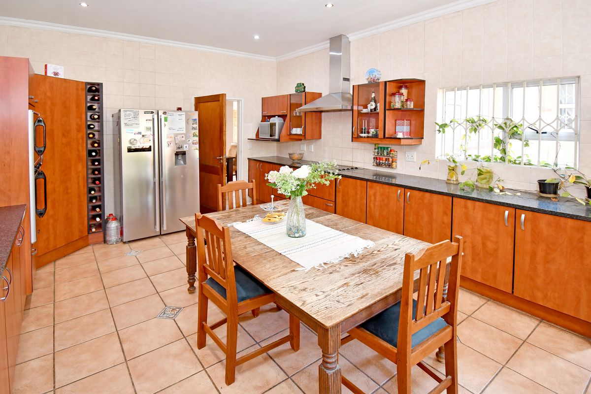 Spacious kitchen featuring wooden cabinetry, granite countertops, stainless steel extractor fan, and tiled flooring with an integrated wine rack.