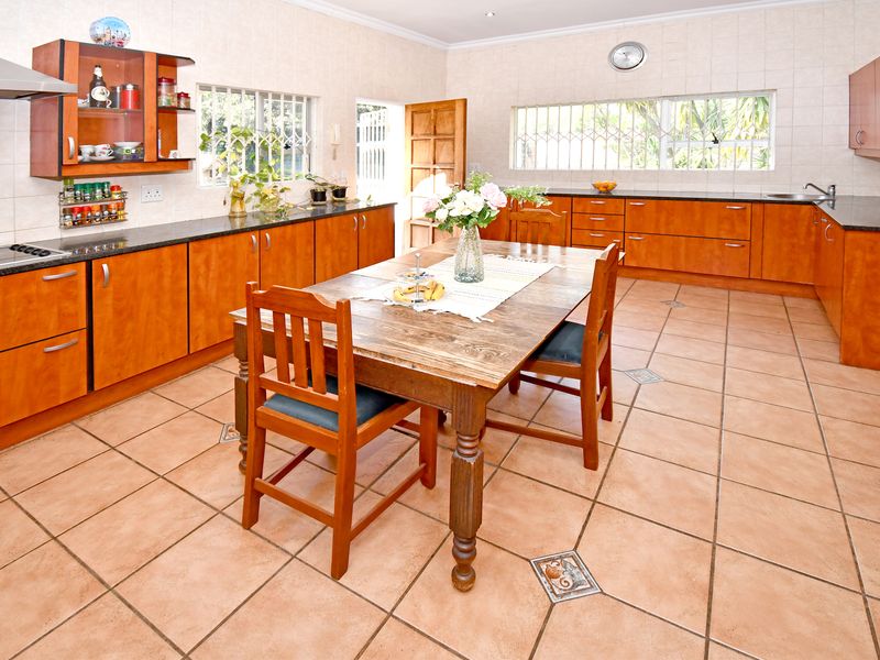Spacious open-plan kitchen and dining area featuring extensive wooden cabinetry, granite countertops, and durable ceramic floor tiles throughout.