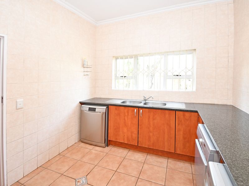 A functional scullery area featuring tiled walls and flooring, granite countertops, and a double bowl sink with built-in cabinetry.