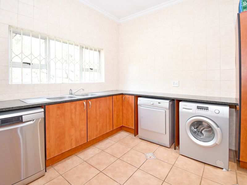 Functional laundry room featuring built-in wooden cabinetry, granite countertops, a double sink, and tiled finishes throughout.