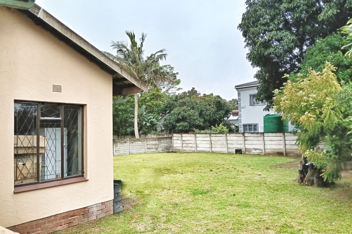 A spacious rear garden featuring a large lawn area, enclosed by a precast concrete boundary wall with an integrated water storage tank.
