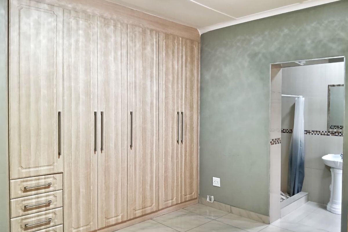 Spacious bedroom featuring extensive built-in cabinetry and an adjoining en-suite bathroom with a pedestal basin and shower.