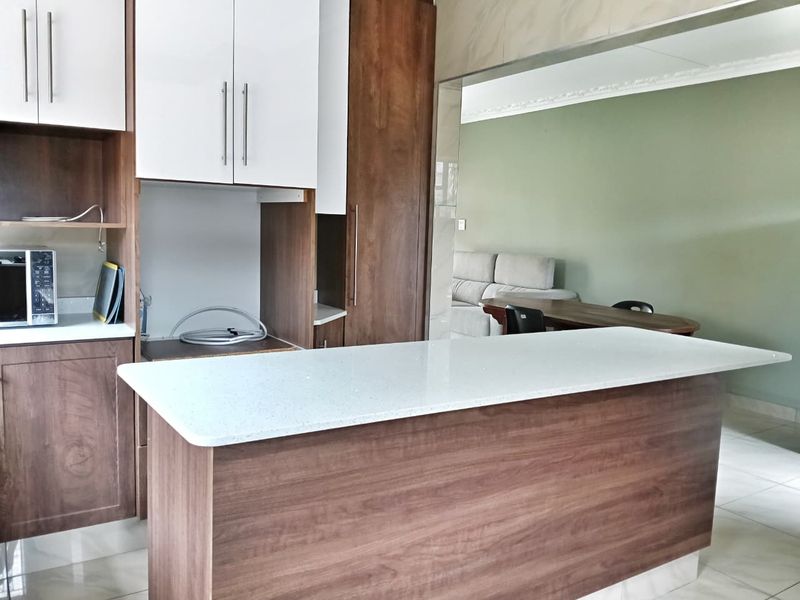 Modern kitchen featuring a central island with stone countertop, two-tone cabinetry, and tiled flooring, seamlessly connecting to the adjacent living area.