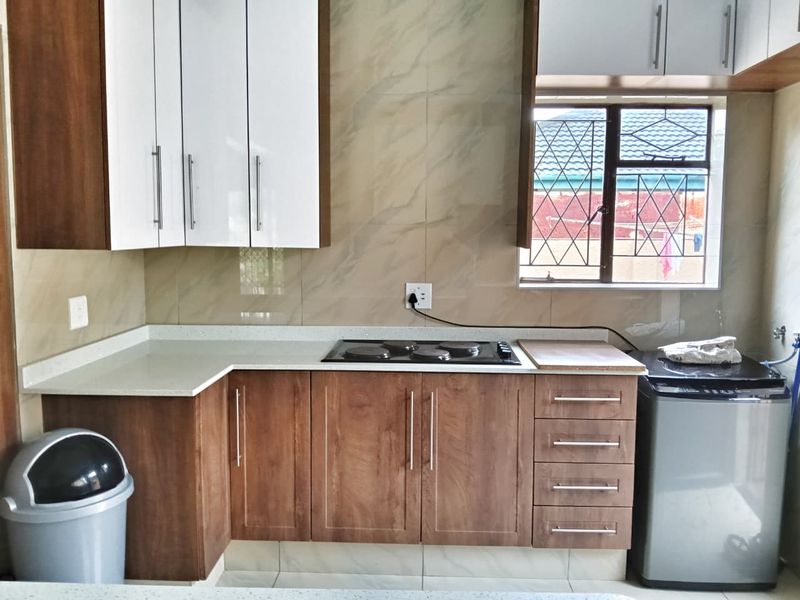 Modern kitchen featuring wood-finish lower cabinets, white upper cabinets, stone countertops, and a built-in electric hob with tiled backsplash.