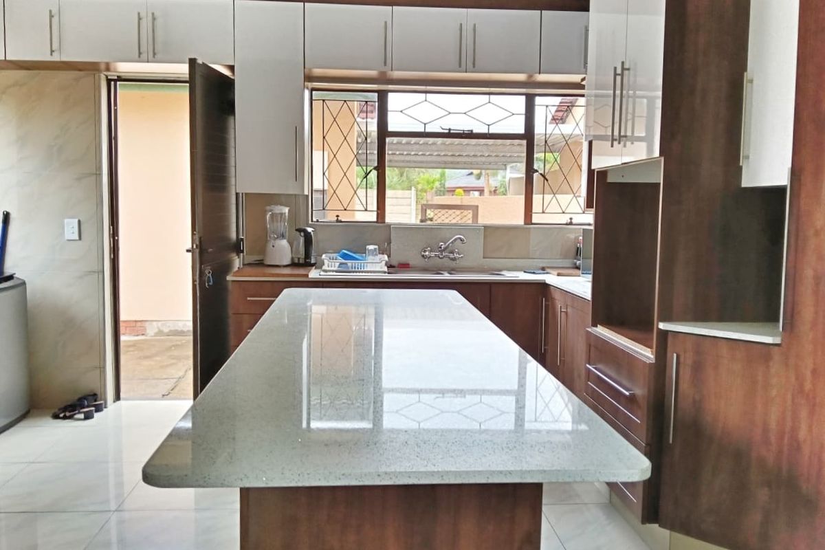A modern kitchen featuring a central island with stone countertops, ample built-in cabinetry, and tiled flooring, with direct access to the exterior.