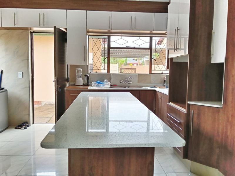A modern kitchen featuring a central island with stone countertops, ample built-in cabinetry, and tiled flooring, with direct access to the exterior.