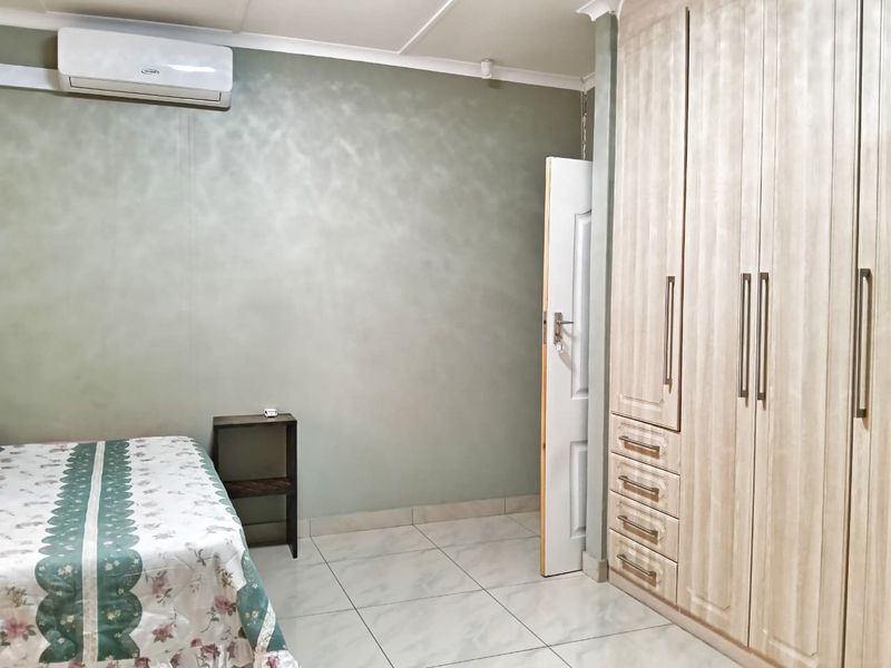 A well-maintained bedroom featuring neutral tiled flooring, ample built-in cupboard storage, and a wall-mounted split-system air conditioning unit.