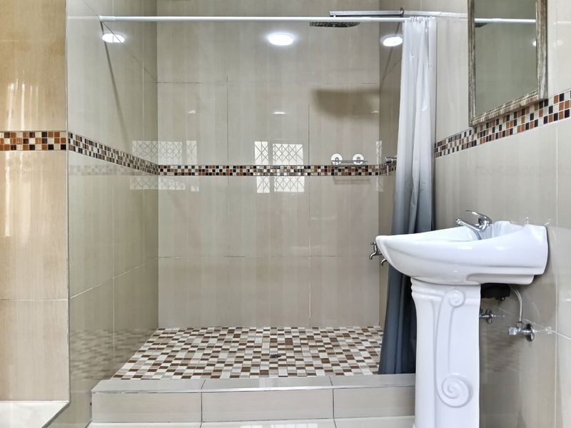 A clean, modern bathroom featuring a walk-in shower with mosaic tile accents and a classic pedestal washbasin.
