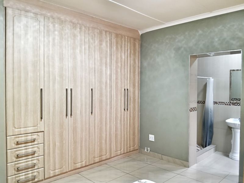 Spacious bedroom featuring extensive built-in cabinetry and an adjoining en-suite bathroom with a pedestal basin and shower.